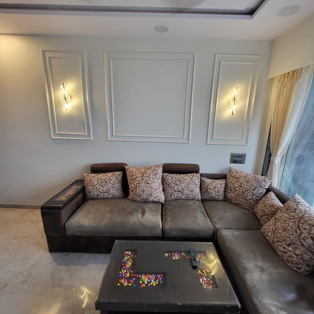 Living room wall with moulded panel detailing, wall sconces, and a cushioned sofa